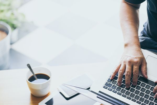 Cookie-Banner: Ausschnitt rechte Hand auf Notebook-Tastatur neben Kaffeetasse