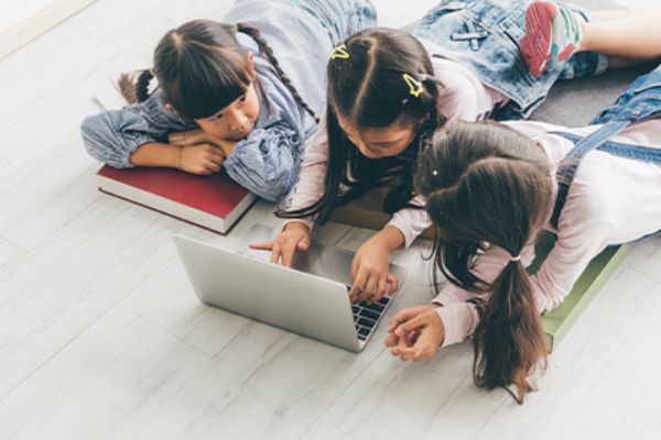 Drei Kinder liegen am Boden und lernen mit einem Laptop für die Schule 