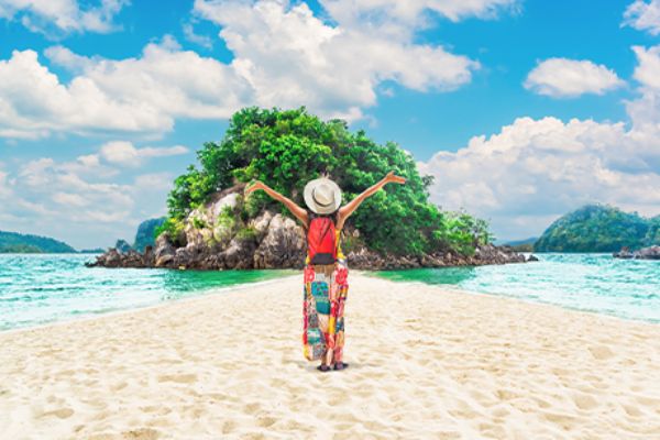 Frau am Strand vor einer Insel und türkisem Wasser