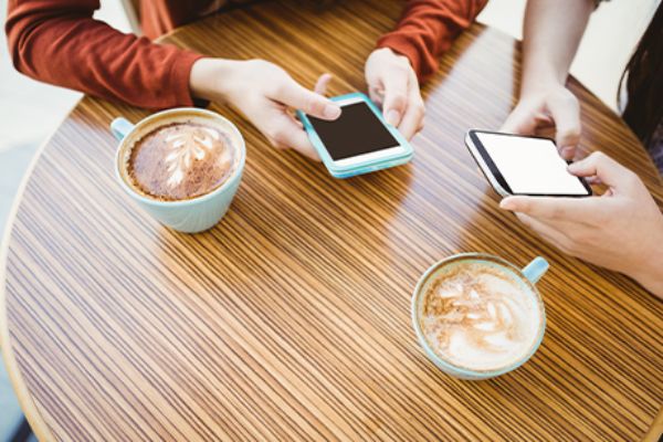 Zwei Personen sitzen vor einem Capuccino mit ihren Smartphones