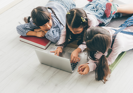 Drei Kinder liegen am Boden und lernen mit einem Laptop für die Schule 