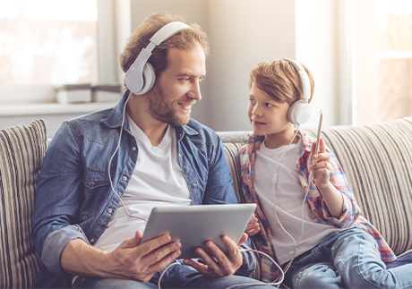 Vater erklärt seinem Sohn sein erstes Handy (auf Couch sitzend)