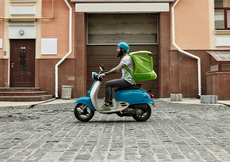 Lieferant auf einem Moped liefert Lebensmittel-Online-Einkauf vor die Tür