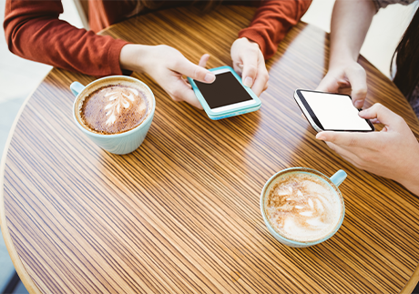 Zwei Personen sitzen vor einem Capuccino mit ihren Smartphones